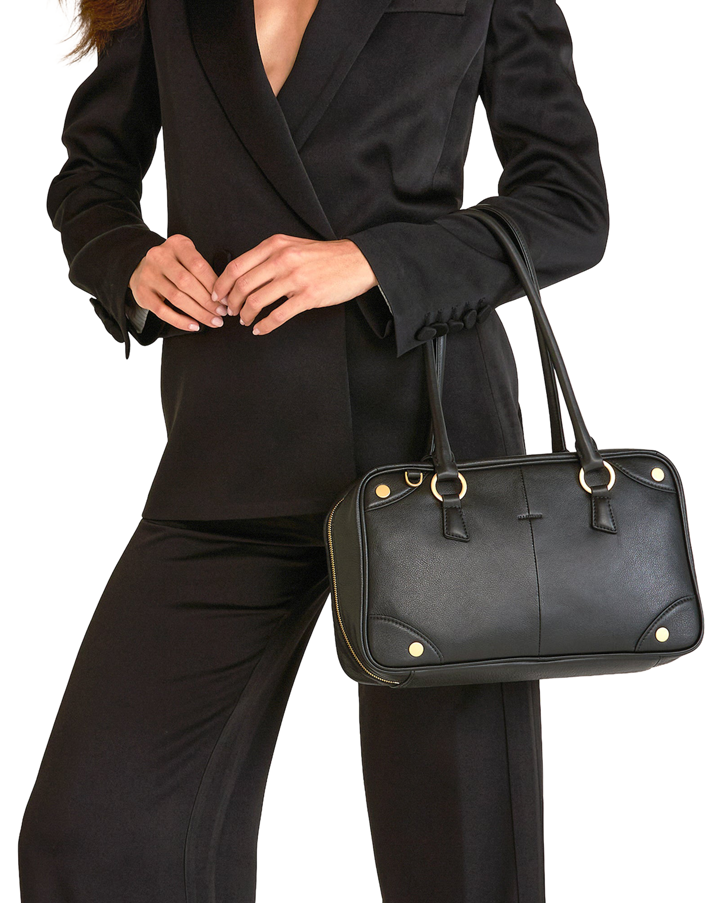 A black leather handbag with gold-tone hardware, carried by a model wearing a black blazer and trousers.