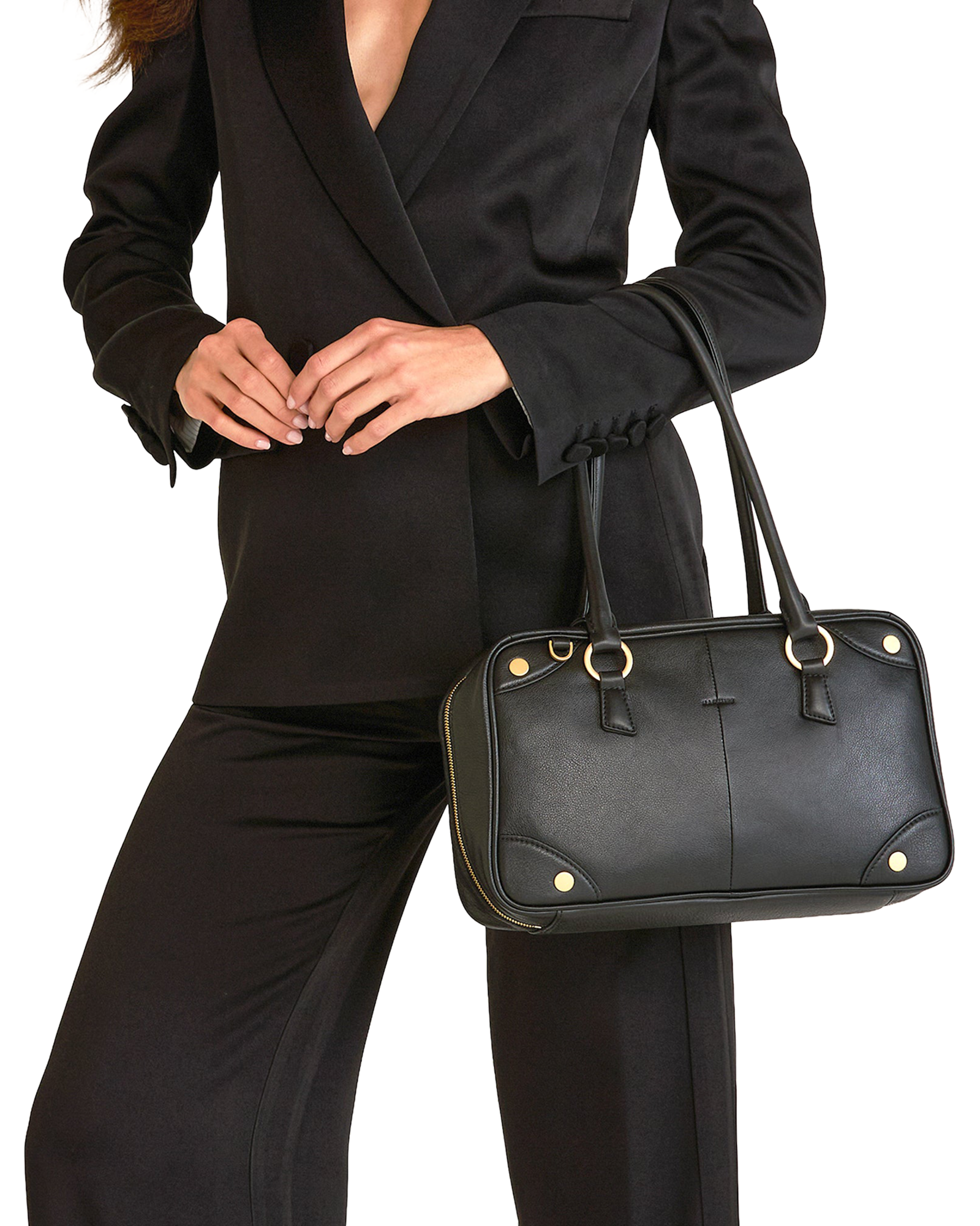 A black leather handbag with gold-tone hardware, carried by a model wearing a black blazer and trousers.