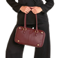 A burgundy leather handbag with gold-tone hardware, held by a model wearing a black blazer and trousers.
