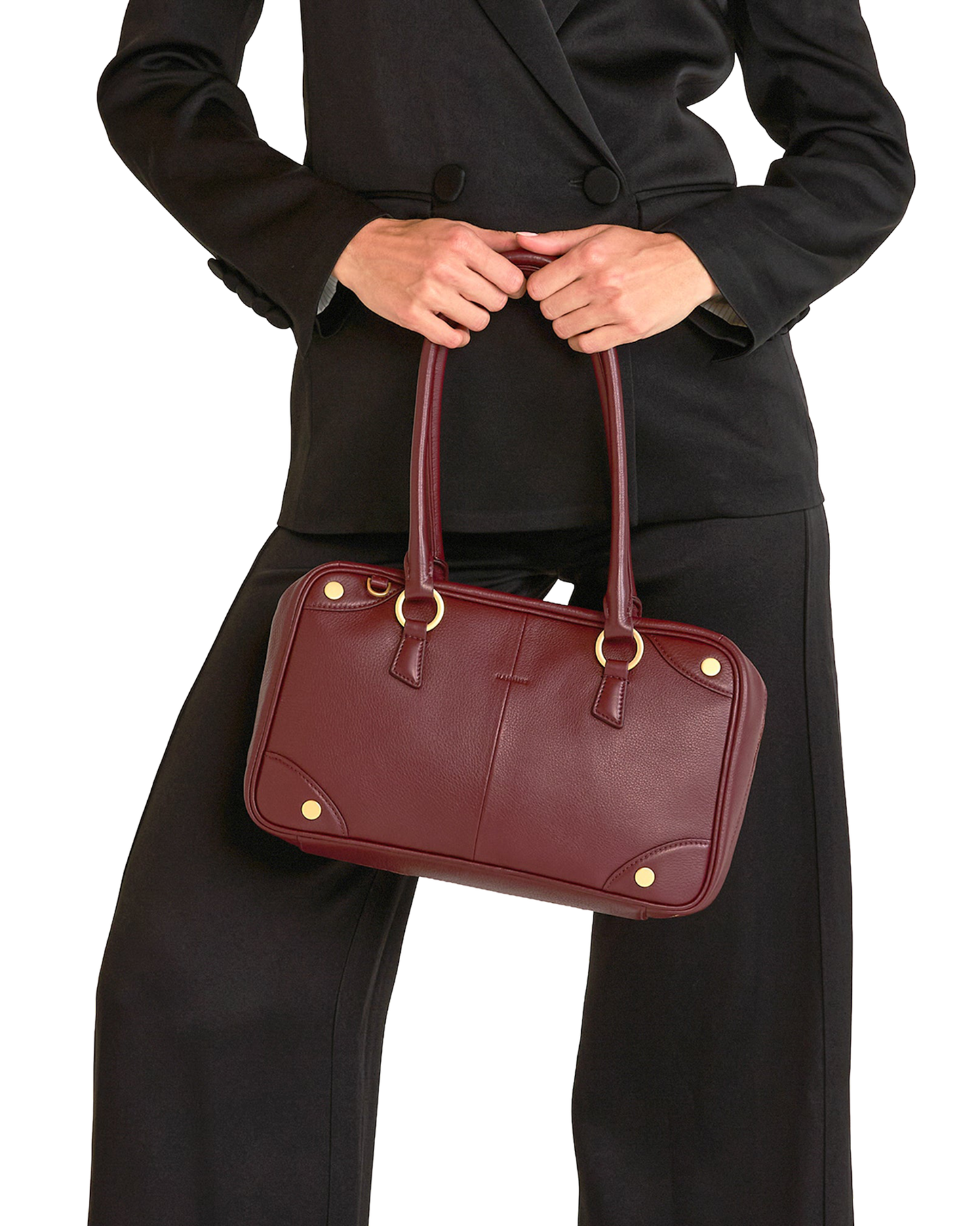 A burgundy leather handbag with gold-tone hardware, held by a model wearing a black blazer and trousers.