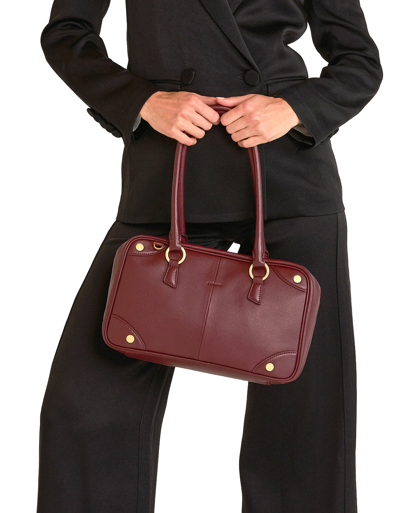 A burgundy leather handbag with gold-tone hardware, held by a model wearing a black blazer and trousers.