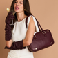 A woman in a cream dress and dark burgundy elbow-length gloves carries a structured burgundy leather handbag with gold-tone hardware.