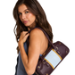 A model with long brown hair wearing a blue dress, carrying a dark plum purple leather shoulder bag with gold-tone hardware and a light blue and gold striped accent panel on the front.