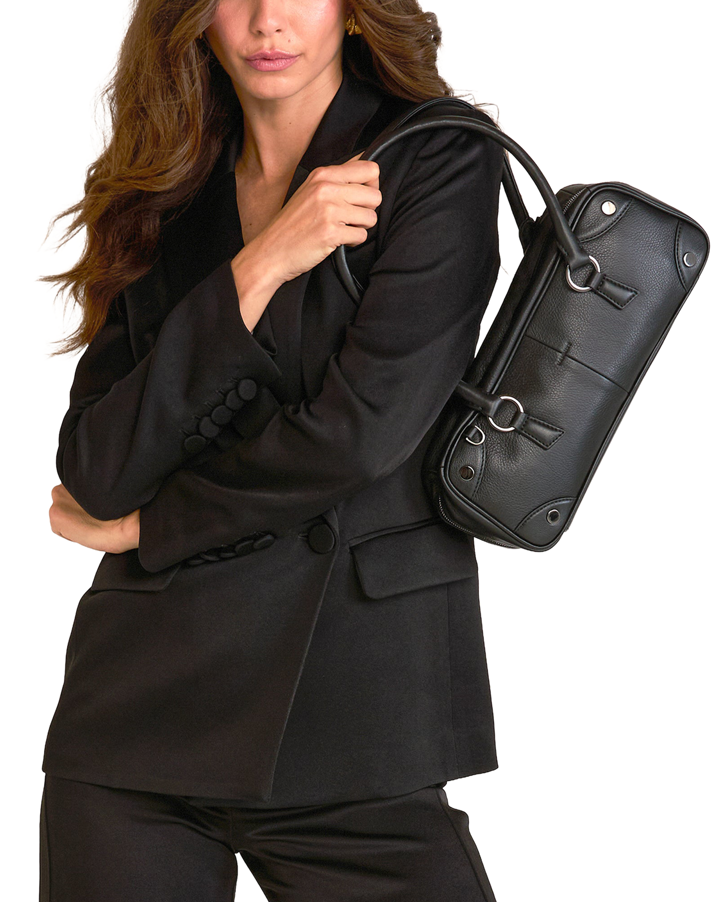 A woman in a black blazer and trousers carries a structured black leather shoulder bag with a top handle.