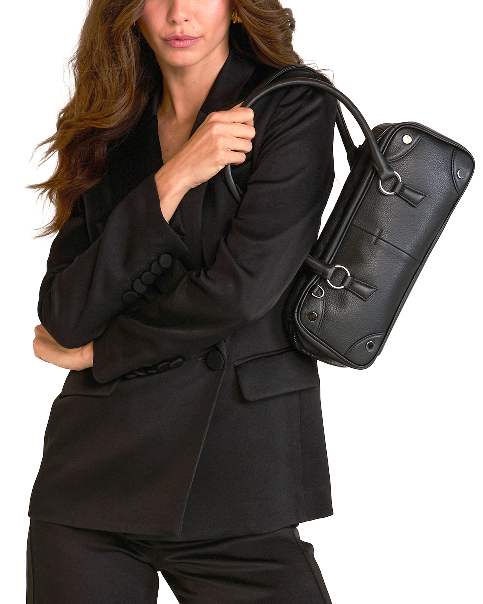 A woman in a black blazer and trousers carries a structured black leather shoulder bag with a top handle.