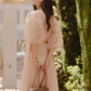 A woman wearing a pale blush pink puff-sleeve midi dress and holding a taupe leather handbag.
