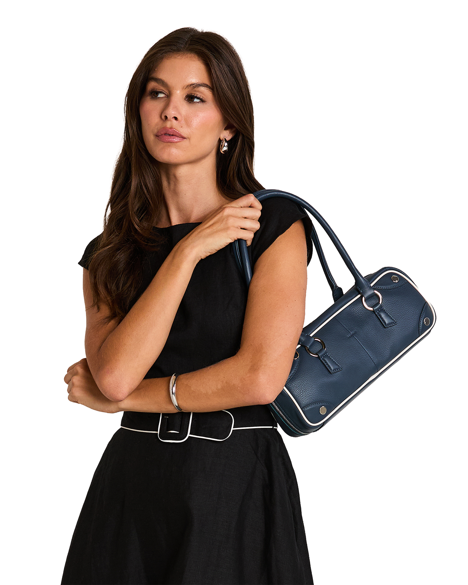A woman in a black sleeveless top and skirt carries a navy blue leather handbag with white piping and silver hardware.