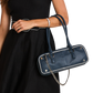 A navy blue pebbled leather handbag with silver-tone hardware and white piping, carried on the shoulder of a model wearing a black dress.