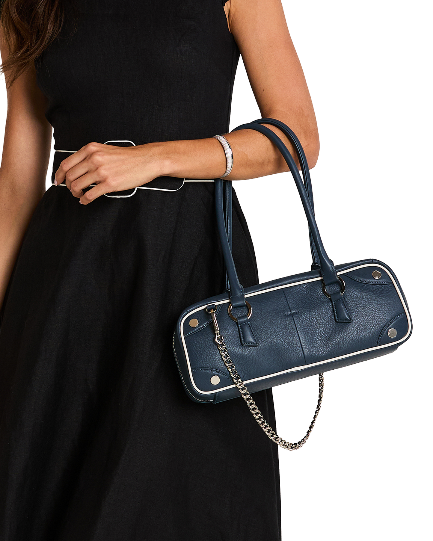 A navy blue pebbled leather handbag with silver-tone hardware and white piping, carried on the shoulder of a model wearing a black dress.