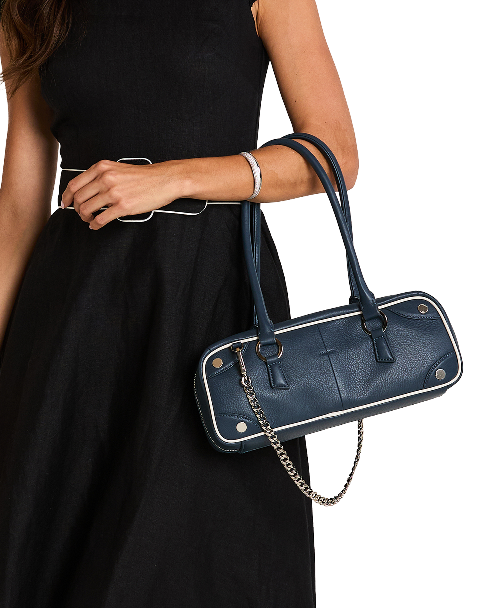 A navy blue pebbled leather handbag with silver-tone hardware and white piping, carried on the shoulder of a model wearing a black dress.