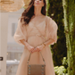 Woman in a light pink dress holding a brown handbag.