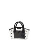 A glossy black and white structured handbag with double top handles and decorative silver-tone studs, shown against a solid black background with a white circular pedestal beneath it.
