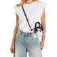 A woman wearing a white sleeveless top and light blue jeans carries a small clear handbag with black handles and a black shoulder strap against a plain white background.