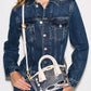 A model wearing a dark blue denim jacket and jeans, carrying a small clear plastic handbag with white handles and trim, styled with white sunglasses inside the bag.