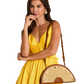 A woman wearing a bright yellow dress and gold earrings carries a brown and beige woven semi-circular shoulder bag with a brown strap.