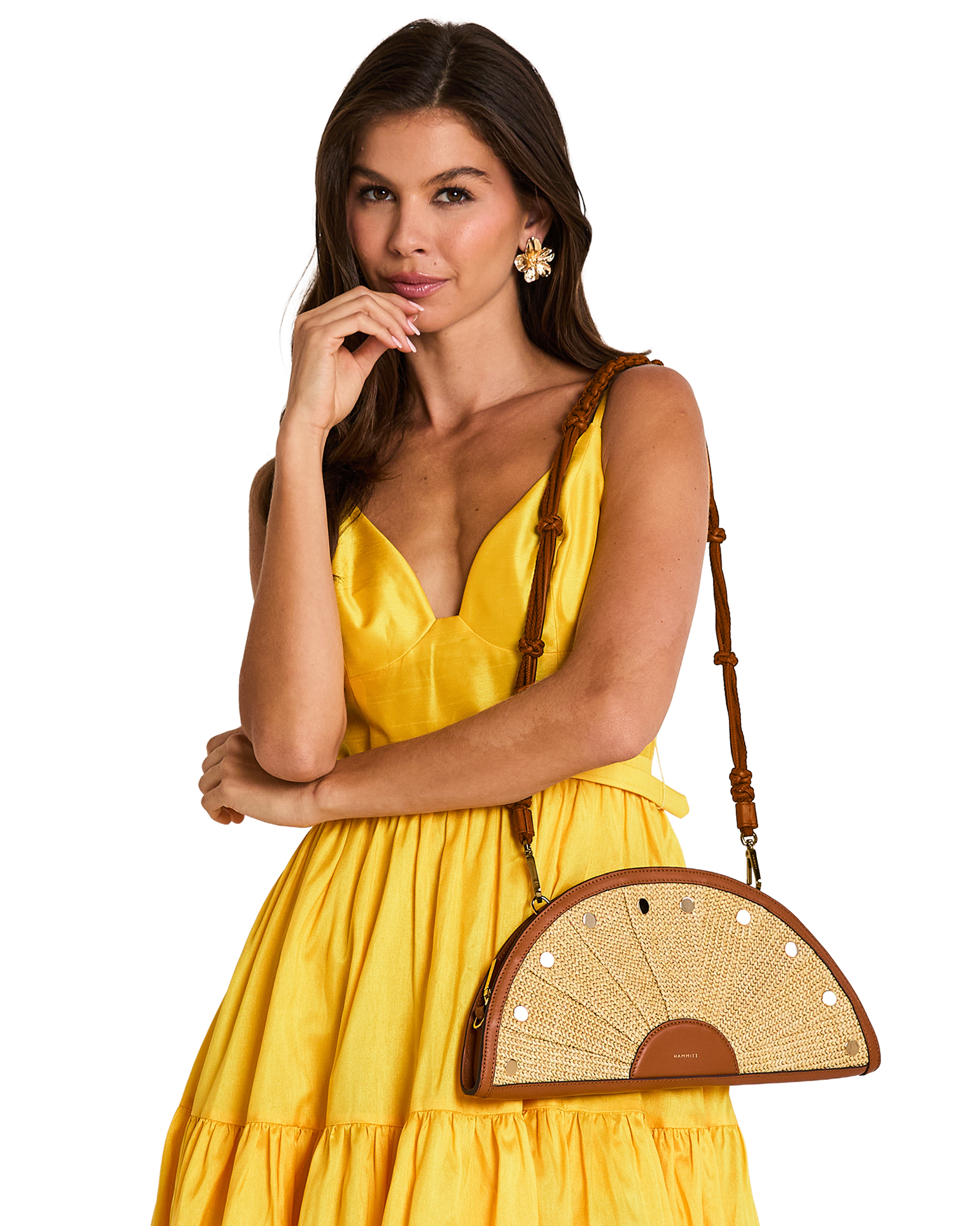 A woman wearing a bright yellow dress and gold earrings carries a brown and beige woven semi-circular shoulder bag with a brown strap.