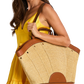 A woman in a yellow dress carries a large woven straw tote bag with brown leather trim and handles.