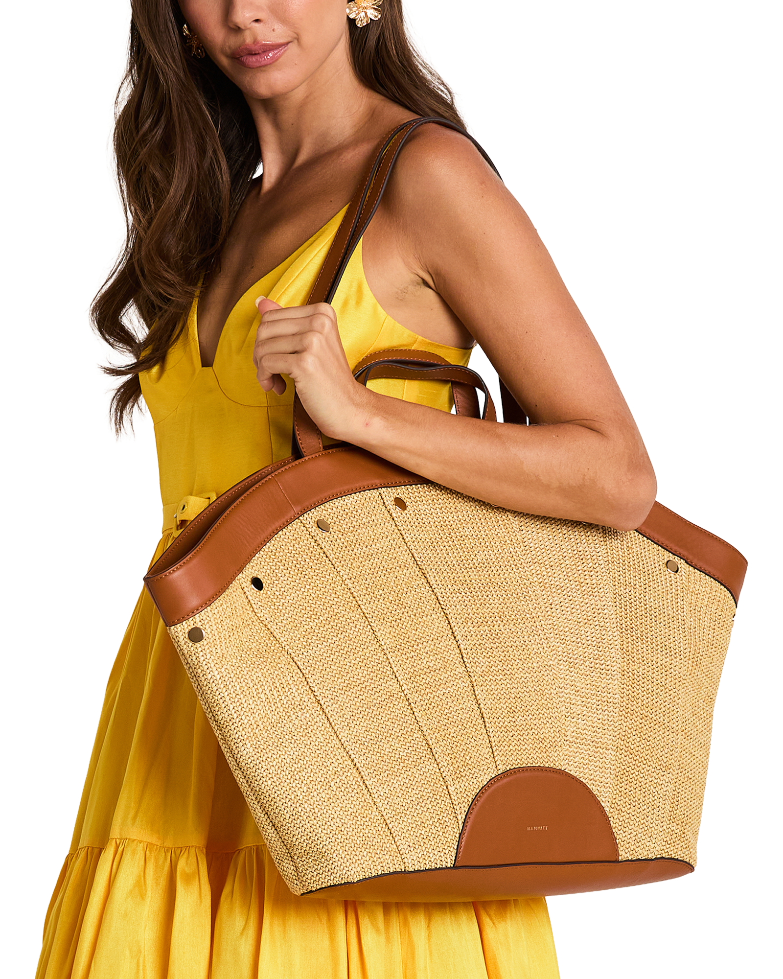 A woman in a yellow dress carries a large woven straw tote bag with brown leather trim and handles.