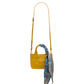 A small yellow leather handbag with a long shoulder strap, top handles, and a blue patterned scarf tied to the handle, shown against a plain white background.