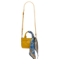 A small yellow leather handbag with a long shoulder strap and a blue patterned silk scarf tied to the top handle, shown against a plain white background.