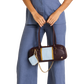 A model wearing a blue jumpsuit holds a dark brown leather handbag with a light blue and yellow color-blocked front panel and a gold chain strap. A small matching light blue pouch hangs from the bag.