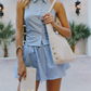 A woman wearing a light blue and white striped sleeveless button-up top and matching striped mini skirt, carrying a large cream shoulder bag and holding a cream clutch with gold studs.