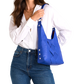 A woman wearing a white button-down shirt and blue jeans carries a bright blue leather shoulder bag with a woven pattern on the front.
