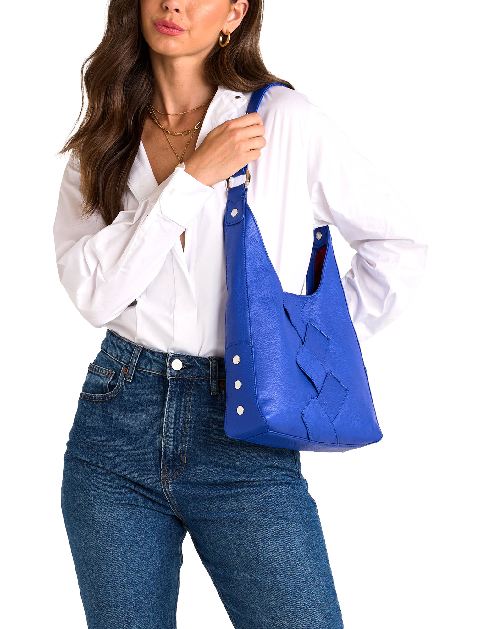 A woman wearing a white button-down shirt and blue jeans carries a bright blue leather shoulder bag with a woven pattern on the front.