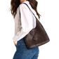 A woman wearing a white blouse and blue jeans carries a large dark brown woven leather shoulder bag against her back.