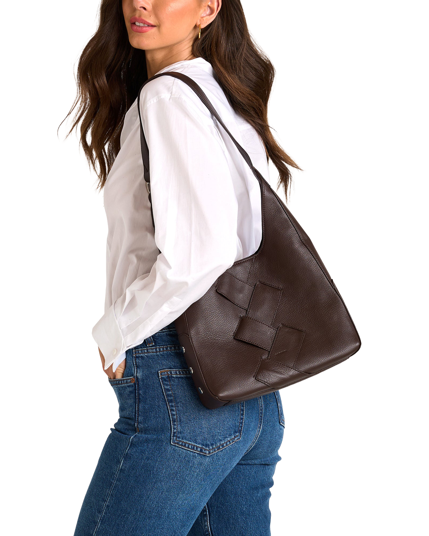 A woman wearing a white blouse and blue jeans carries a large dark brown woven leather shoulder bag against her back.