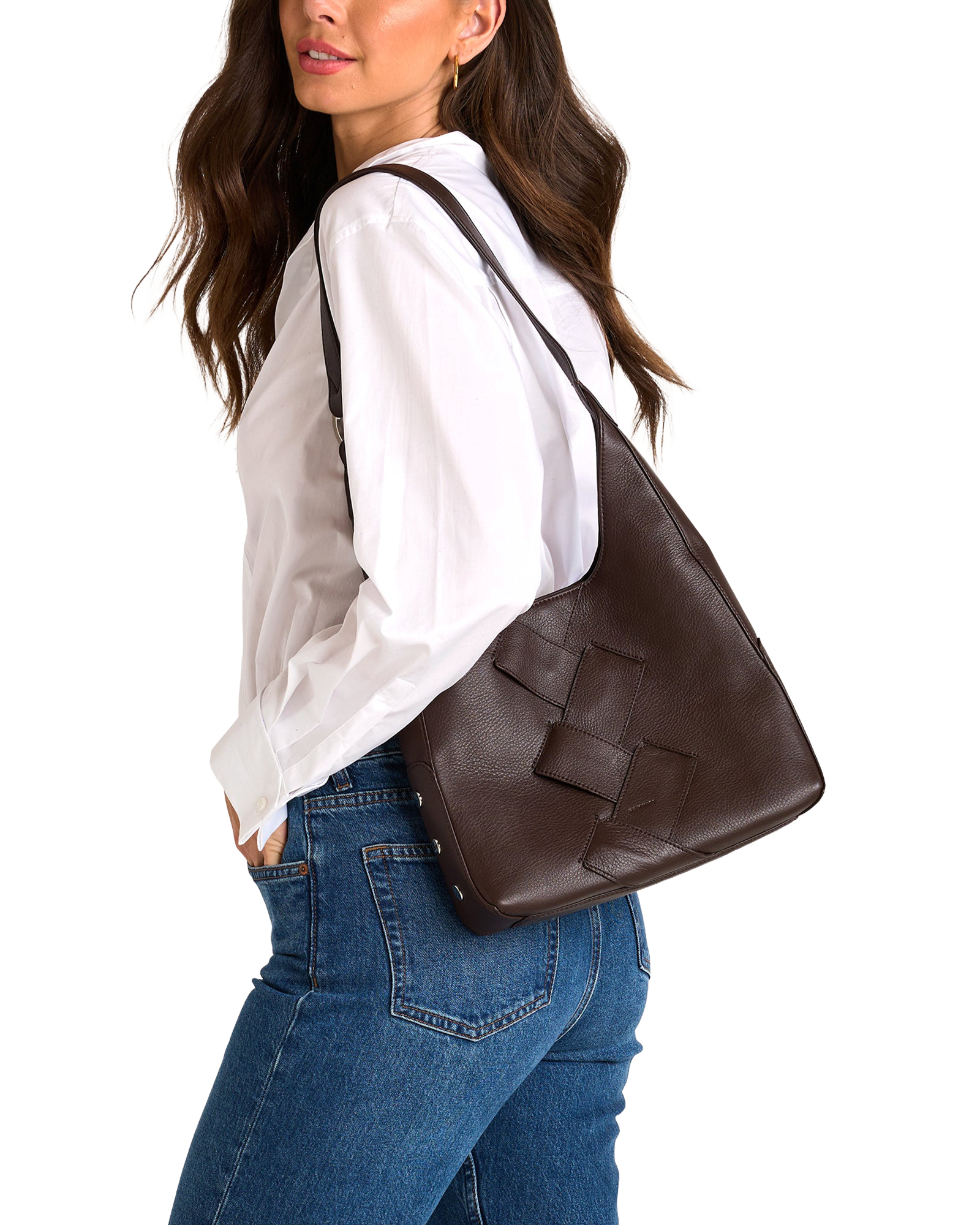 A woman wearing a white blouse and blue jeans carries a large dark brown woven leather shoulder bag against her back.