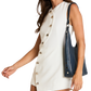 A woman wearing a sleeveless off-white mini dress with gold-tone decorative buttons down the front, styled with a navy-blue shoulder bag.