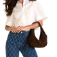 A woman wearing a white short-sleeve button-up shirt and blue patterned jeans, carrying a brown suede shoulder bag.