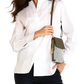 A woman wearing a white button-up blouse and dark pants, holding a small olive green and patterned crossbody bag against a plain white background.