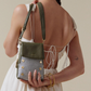 Woman holding a green and black patterned handbag against a neutral background.