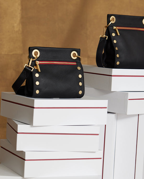 Image onf Tony Sml in black with red and gold zip on top of Hammitt boxes.