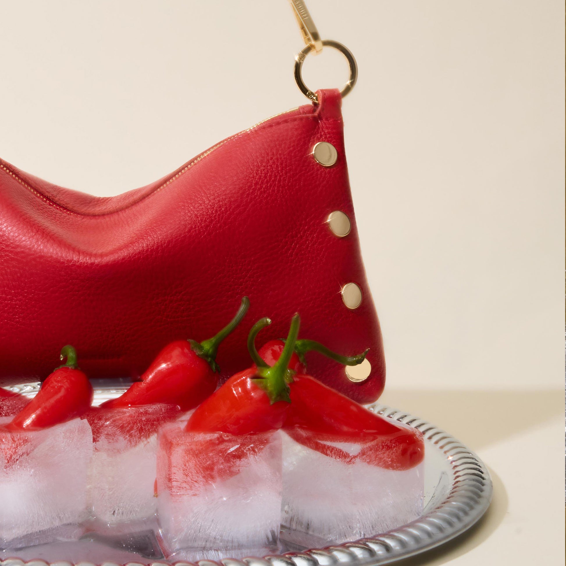 Red leather handbag with gold accents on a tray of ice and red peppers.
