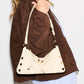 A cream-colored shoulder bag with gold-tone hardware and a thin strap, worn crossbody under a brown suede jacket by a model.