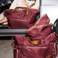 A set of three burgundy nylon duffel bags with tan leather handles and trim, displayed on the ground and in the trunk of a silver car next to a woman.