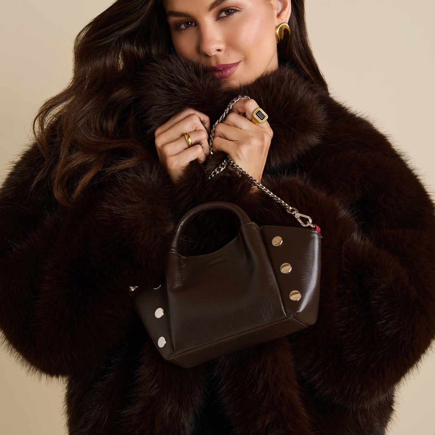 Woman holding a brown handbag with a fur coat against a beige background