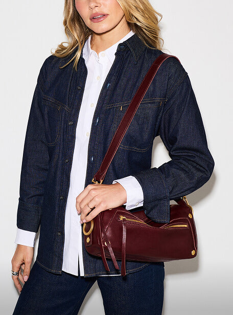 A woman wearing a dark blue denim shirt-jacket over a white collared shirt, carrying a burgundy leather shoulder bag with gold hardware.