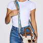 A model wearing a white t-shirt and blue jeans carries a small clear handbag with brown leather handles and a blue patterned scarf against a light gray background.