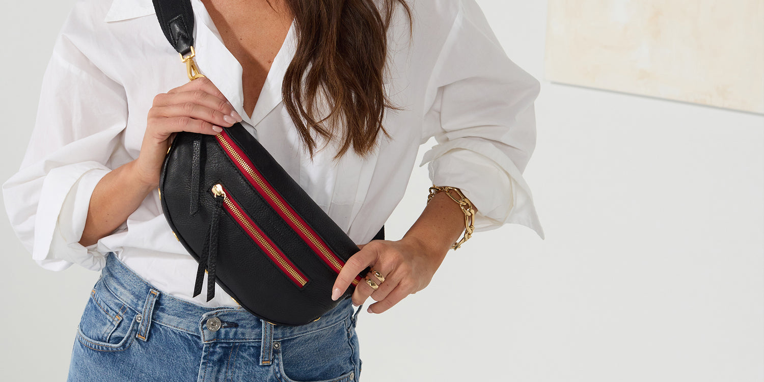 Image of model in white top and blue jeans wearing charles in black brushed gold red zip as crossobody.