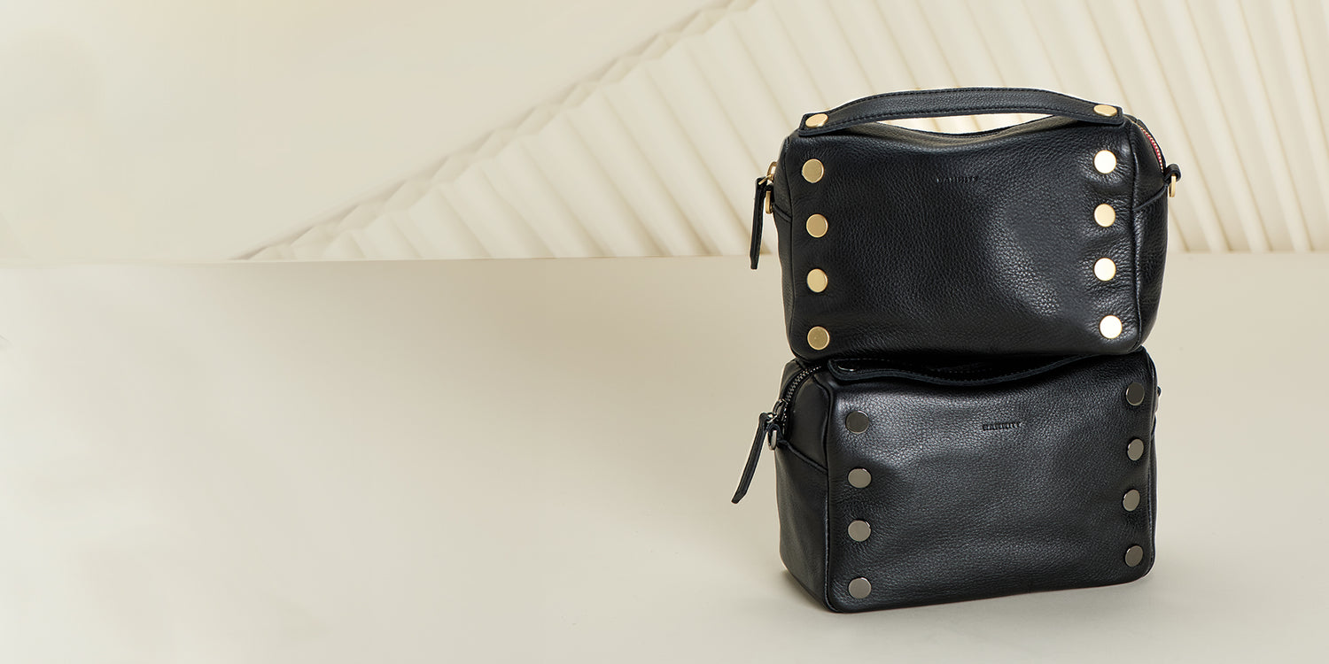 Image of two Evan bags on white backdrop. One Evan crossbody in black burshed gold and second evan crossbody in black gunmetal.