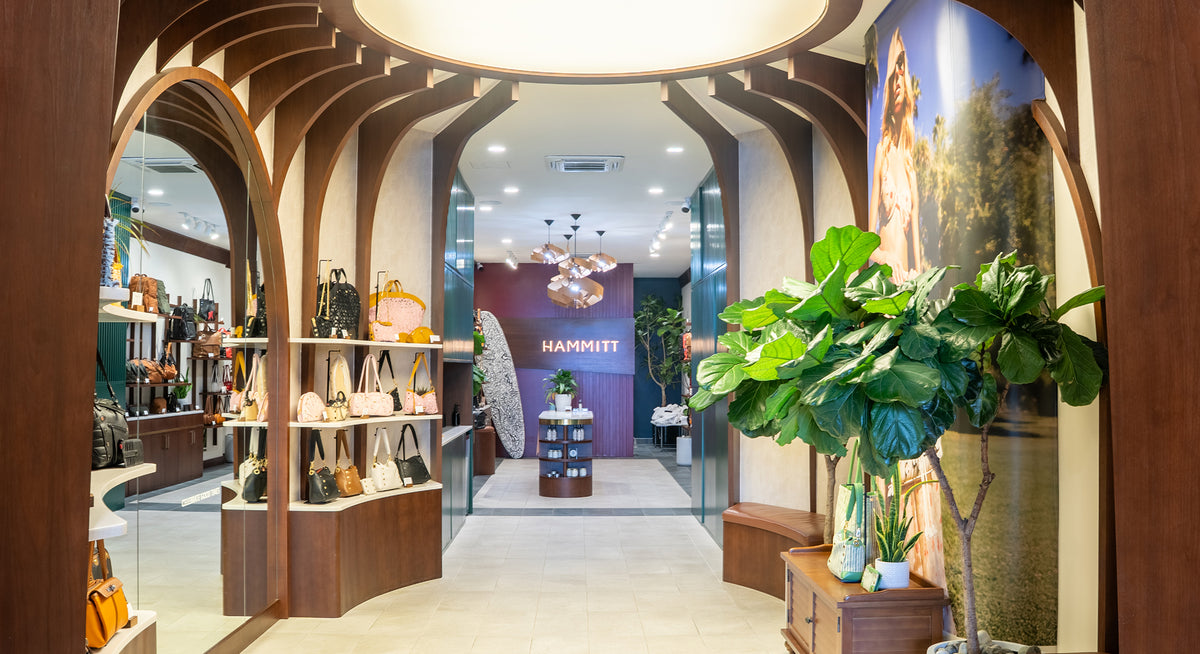 A luxury boutique interior with wooden arched display frames, a large green potted plant in the foreground, and a visible HAMMITT brand display in the distance.