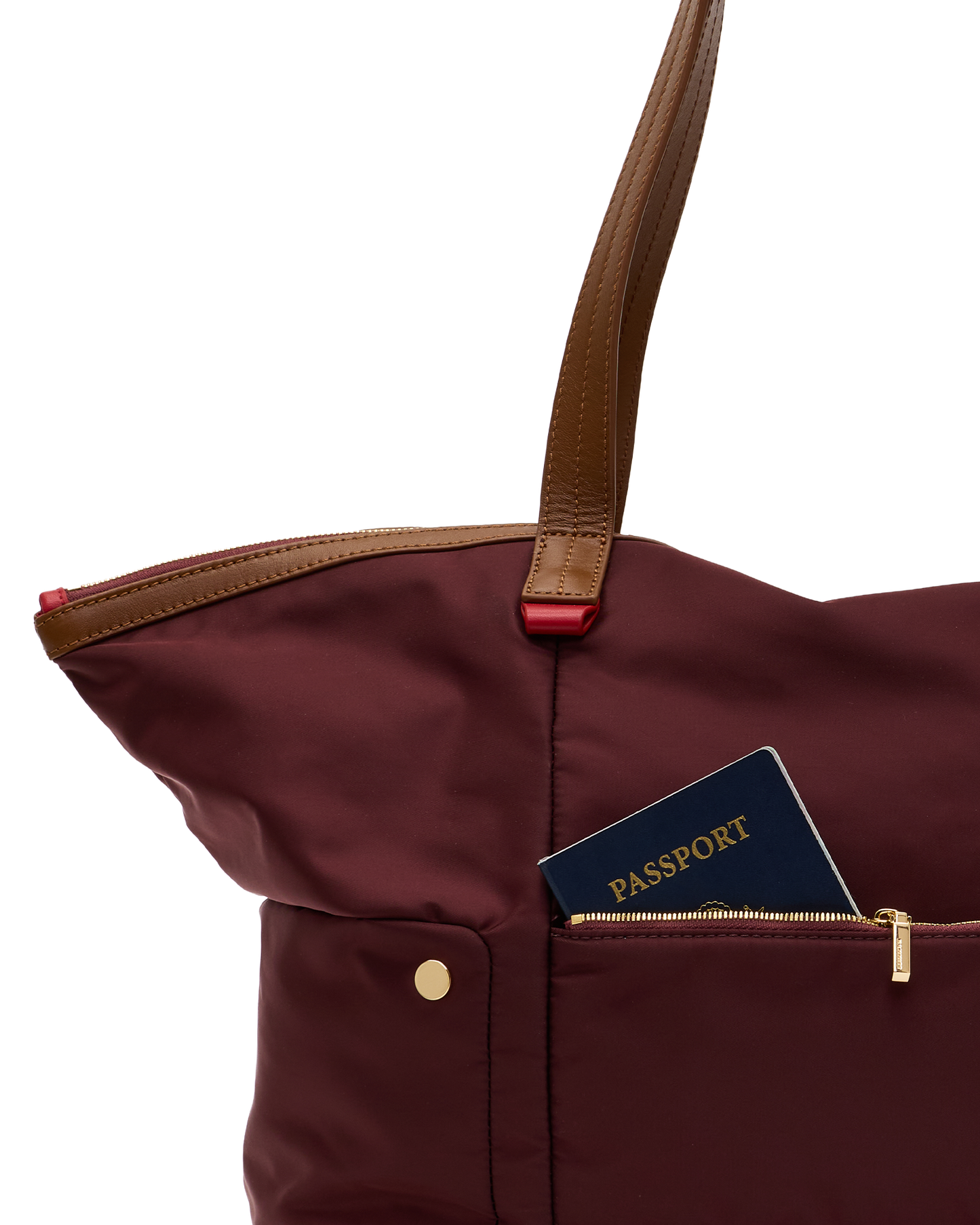 A close-up of a burgundy nylon tote bag with brown leather handles and a front zip pocket holding a navy blue passport, set against a plain white background.