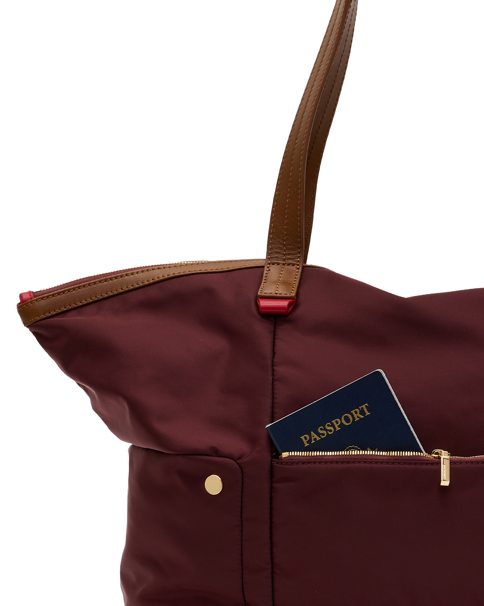 A close-up of a burgundy nylon tote bag with brown leather handles and a front zip pocket holding a navy blue passport, set against a plain white background.
