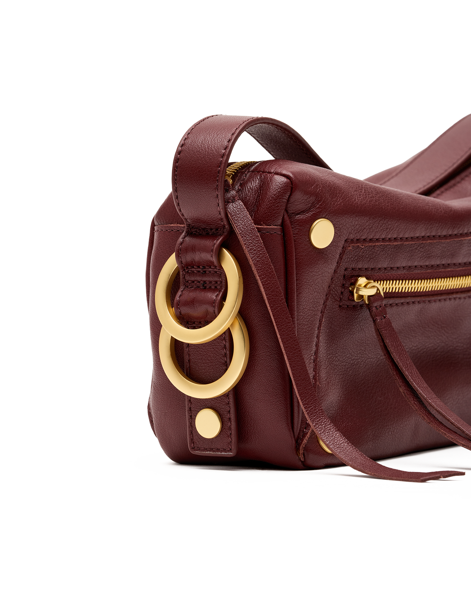 A close-up of a dark burgundy leather handbag featuring large gold-tone double rings and gold hardware on a white background.