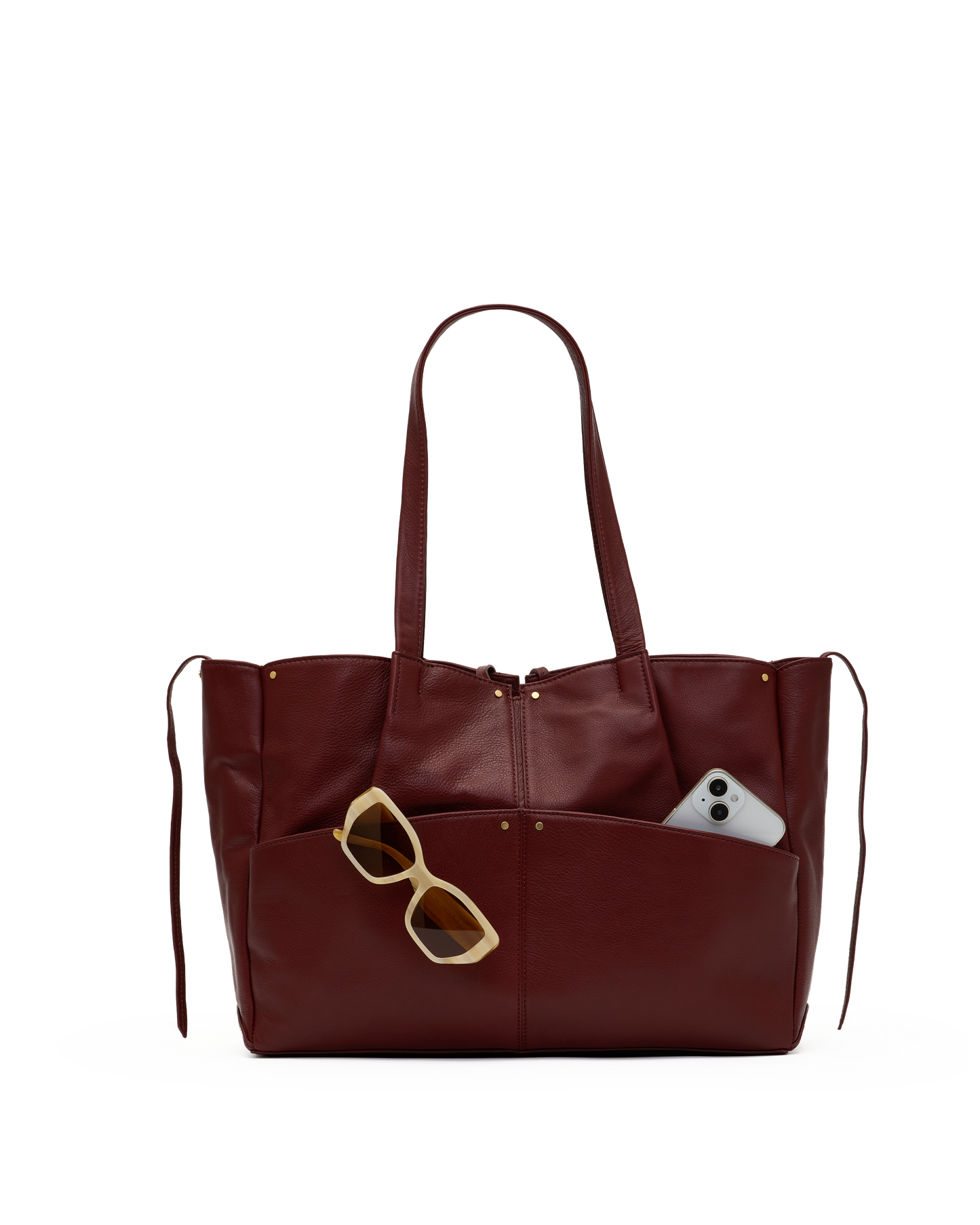A burgundy leather tote bag with dual shoulder straps and a front slip pocket containing tortoiseshell sunglasses and a smartphone, shown on a plain white background.