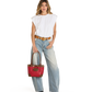 A woman modeling a white sleeveless top, light-wash wide-leg jeans, a brown belt, and black boots, holding a red leather handbag with brown leather handles and trim against a plain white background.